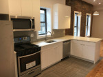 Modern kitchen in renovated studio apartment with stone countertops and stainless steel appliances.