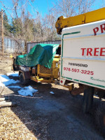 1989 F700 Versalift truck with a green tarp in a wooded area, used locally and well maintained.
