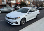 2019 Kia Optima LX sedan in pearl white color parked on the street, featuring alloy wheels and a sleek design.