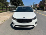 Front view of a white 2016 Kia Sedona L parked on a city street, showcasing its modern design.