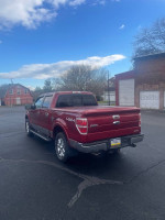 2013 Ford F-150 Lariat 4WD in red, parked with a clean exterior, showcasing the hard tonneau cover and chrome wheels.