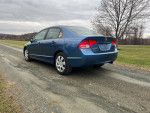 2008 Honda Civic LX in blue color parked on gravel road with green field backdrop, showcasing rear view.