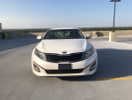 Front view of a 2015 Kia Optima parked in an open area with a clear sky and distant landscape.