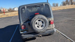 Rear view of a 2002 Jeep Wrangler parked, showing tire and mild wear details.