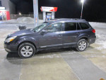 2012 Subaru Outback Limited parked at a gas station, showcasing its sleek design and snow-covered surroundings.