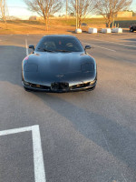 Front view of a black Chevrolet Corvette with aftermarket wheels in a parking lot.