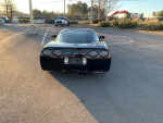 Rear view of a black Chevrolet Corvette with aftermarket exhaust, parked in a lot, highlighting its sleek design.