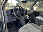 Interior view of a 1999 Chevrolet Express 3500 with grey seats and dashboard, showing wear and storage features.