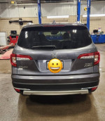 Rear view of a 2019 Honda Pilot Touring in bluish-grey color, parked in a workshop with tools in the background.
