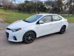 2016 Toyota Corolla S in white, showcasing sporty design, parked on a gravel road with green grass background.