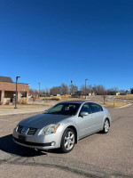 2005 Nissan Maxima parked in a suburban area under a clear blue sky with new tires and recent maintenance.