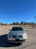Front view of a silver 2005 Nissan Maxima parked outdoors against a clear blue sky.