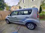 2011 Kia Soul with 85,000 miles, silver exterior, parked in a driveway with wooden fence background.
