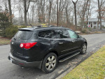2009 Chevrolet Traverse LTZ AWD parked on a tree-lined street, showcasing its sleek black design and spacious rear.