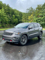 Gray Jeep Grand Cherokee Trailhawk parked on a wet road surrounded by green trees
