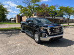 2021 GMC Sierra 1500 Denali 4WD in black parked with clear sky and trees, showcasing its sleek design and features.