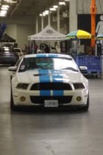 Front view of a classic Shelby GT500 with blue stripes parked indoors, featuring a modified engine and custom suspension.