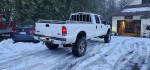 White 2001 Ford F350 truck with 8" lift and oversized tires in snowy driveway