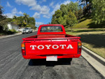 Red 1983 Toyota Pickup parked on street, showcasing back view with clear Toyota logo.