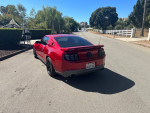 2010 Ford Mustang GT in red with aftermarket mods parked on the street, showcasing its sporty design.