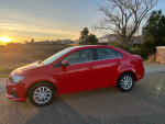 Red 2018 Chevrolet Sonic LT parked with a sunset backdrop, showcasing its sleek design and efficient features.