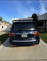 Rear view of a 2020 Infiniti QX80 SUV parked in a driveway, showcasing its sleek design and spaciousness.