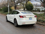 2021 Tesla Model 3 in pearl white with Autopilot and full self-driving features parked in a leafy area.