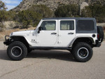2007 Jeep Wrangler JK with upgrades and new tires, parked on a gravel road in a natural setting.