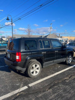 2012 Jeep Patriot AWD parked, featuring new tires and a towing package, in excellent condition under a clear sky.