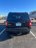 Rear view of a 2012 Jeep Patriot with a black exterior parked in a lot, showcasing its towing package and clean design.