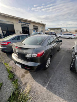 2010 Mazda 3 parked at a service shop, showing wear from sun and mechanical issue, available for cash sale.