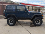 2000 Jeep Wrangler Sport 4WD with aftermarket upgrades, parked at a gas station.