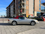 2000 Mercedes-Benz SL500 with burgundy soft top parked near modern buildings, featuring low mileage and clean title.
