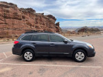 Side view of a 2013 Subaru Outback parked near rocky mountains, showcasing its adventure-ready design.
