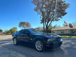 2012 Ford Mustang V6 in black, parked on a street, showcasing its sporty design and shiny exterior.