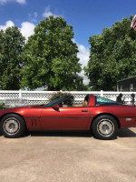 1987 Chevrolet Corvette in red, parked outside with trees in the background, showcasing its original design.
