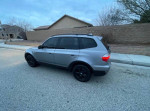 2009 BMW X3 SUV in silver color, parked on the street with a panoramic sunroof and tinted windows.
