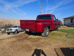 Red 1975 Chevy C10 Stepside truck parked on grassy land with a scenic view.