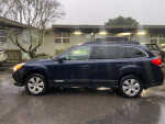 2012 Subaru Outback 2.5L Premium in dark blue parked on a rainy street, highlighting its sleek design and all-wheel drive features.