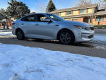 2016 Kia Optima in silver parked on snow-covered street, featuring clean body and stylish design.