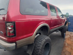 2000 Ford Excursion with V10 engine, red exterior, and large tires in towing yard, ready for sale.