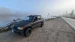 2002 Kia Sportage 4x4 lifted SUV with aftermarket features parked by a foggy lakeside road.