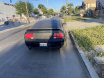 Back view of a black 2006 Ford Mustang GT parked on the street with minor scratches and clean title.