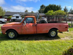 1968 Chevrolet C10 pickup truck in orange with a long bed, vintage styling, parked on grass.