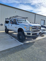 2016 Ford F250 Super Duty truck with 6" lift and aftermarket rims parked outside a building.