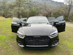 Front view of a 2018 Audi A5 Prestige AWD hatchback with open doors parked in a scenic outdoor setting.