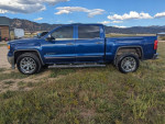 2014 GMC Sierra 1500 SLT 4WD in cobalt blue with chrome wheels parked on grassy terrain