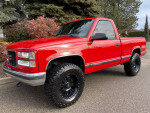 1997 GMC Sierra 1500 SL 4WD in red with matte black wheels, standing on a pavement surrounded by greenery.