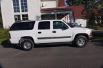 2005 Chevrolet Suburban LS 4WD in white exterior, parked by a house, showcasing its spacious design and features.