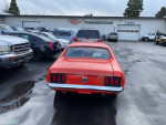 Orange 1970 Ford Mustang parked with various cars, showing its rear and new rims.